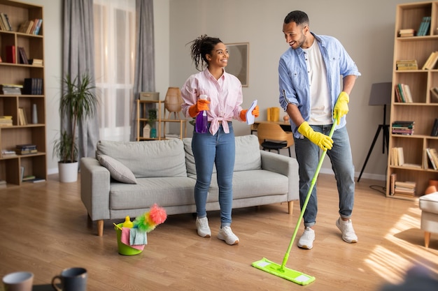 Photo cheerful black spouses cleaning living room doing housework at home