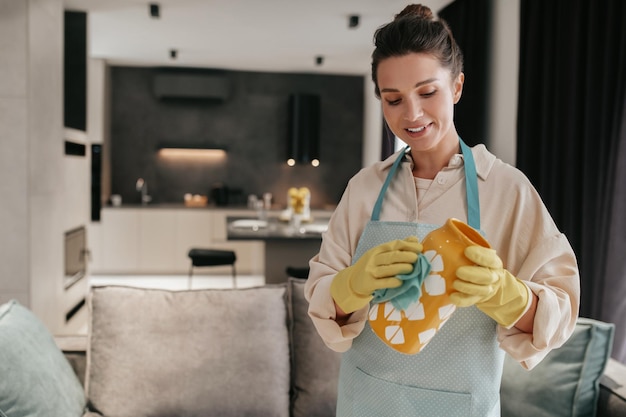 Free photo cleaning crockery. a woman in gloves cleaning an orange vase