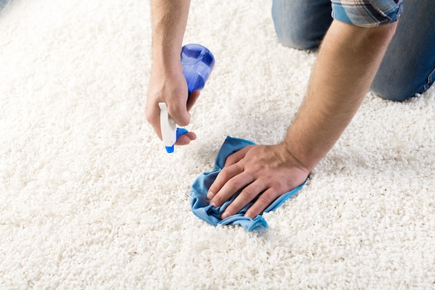 Photo cleaning and home concept - close up of male cleaning stain on carpet with cloth