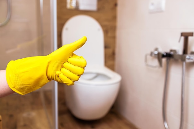 Photo closeup of a hand in a yellow glove on the background of the bathroom