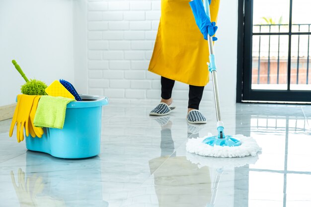 Photo happy young woman in blue rubber using mop while cleaning on floor at home