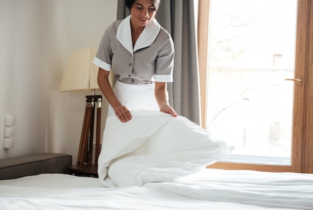 Free photo maid setting up white bed sheet in hotel room