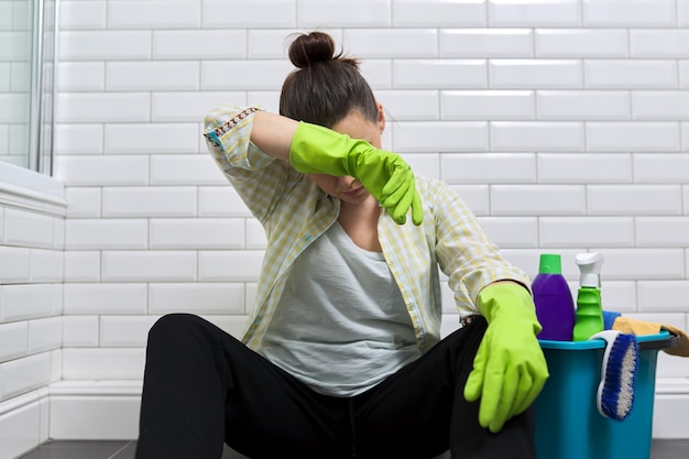 Foto mulher cansada, fazendo a limpeza da casa no banheiro. mulher em luvas com detergentes, balde sentado no chão. fadiga, estresse, limpeza, casa