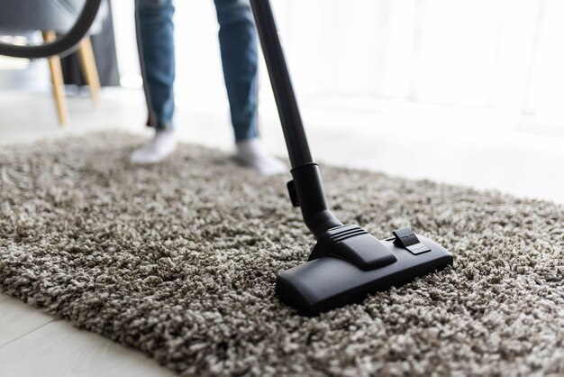 Free photo people, housework and housekeeping concept - close up of woman with legs vacuum cleaner cleaning carpet at home