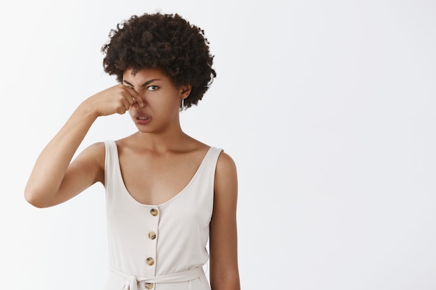 Free photo portrait of displeased intense disappointed african american funny woman with afro hairstyle covering nose with fingers frowning from dislike