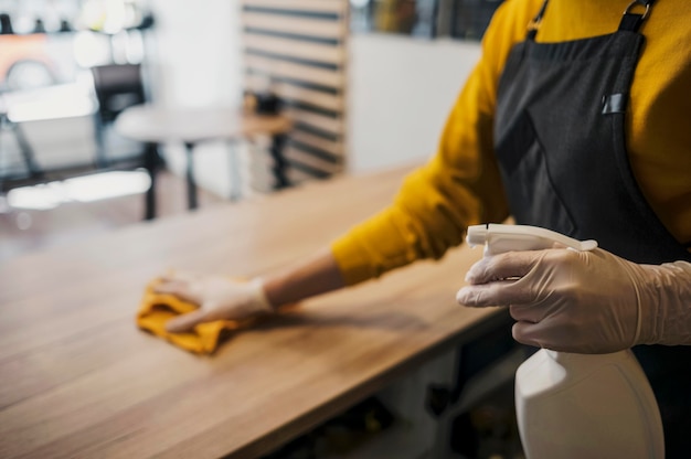 Free photo side view of female barista cleaning table while wearing latex gloves