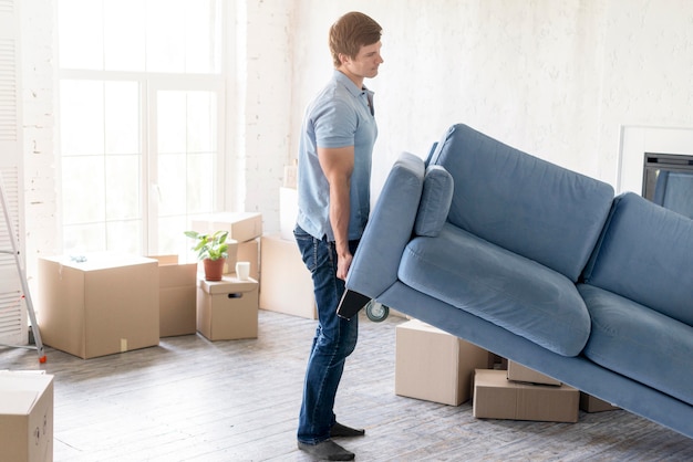 Free photo side view of man handling couch while preparing to move out