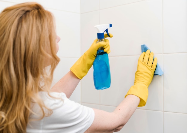 Free photo side view of woman cleaning the shower wall