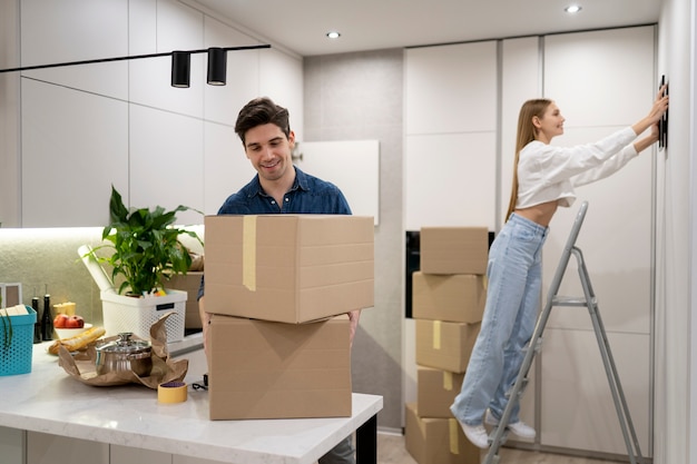 Free photo woman hanging frame on the wall while her boyfriend is handling boxes