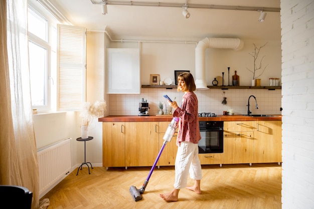Photo woman vacuuming floor with a cordless hand vacuum cleaner in kitchen