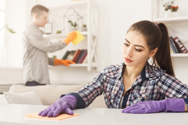 Photo young couple in rubber gloves cleaning home, wiping dust with towel in living-room, copy space, selective focus. housekeeping and cleaning service concept