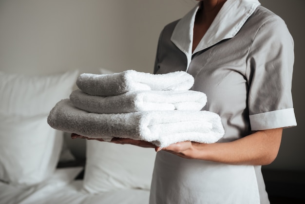 Free photo young hotel maid standing and holding fresh clean towels